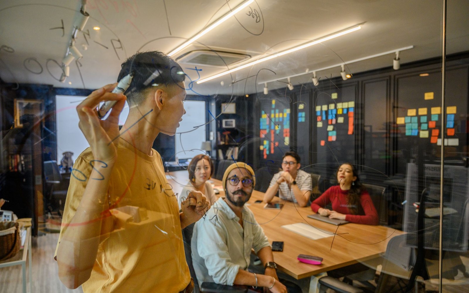 Adults seated around a table in a glass-walled meeting room