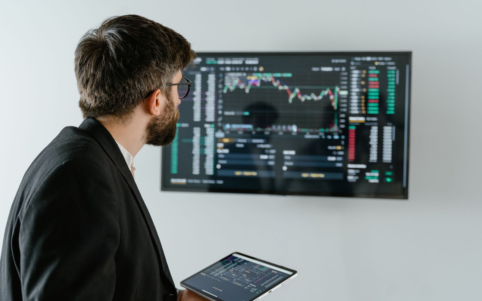 Adults at trading terminals on a listing morning, mid-reaction — faces visible, screens reflecting green and red figures